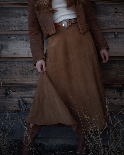 Person wearing a brown coat and skirt against a wooden wall.