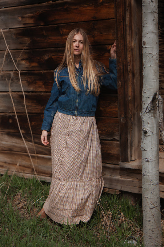 Person wearing a blue jacket and beige skirt standing in front of a wooden cabin.
