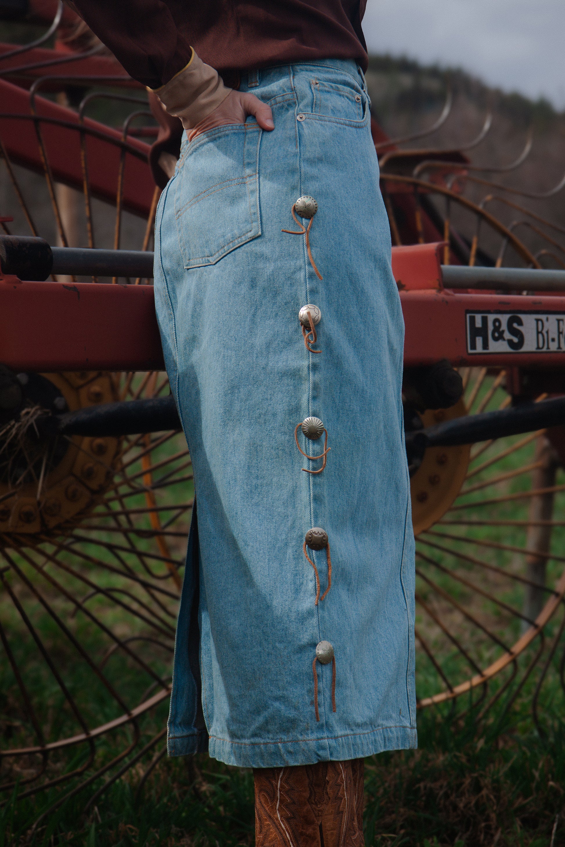 Person wearing a long blue denim skirt with buttons standing next to a large agricultural machine.