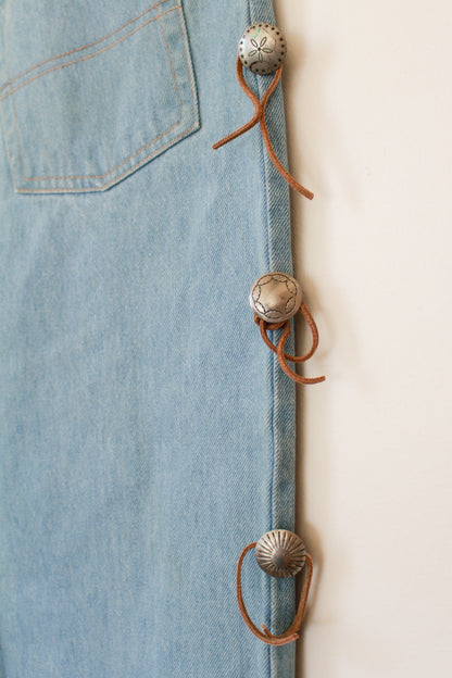 Close-up of a denim jacket with decorative buttons and leather strap on a light background