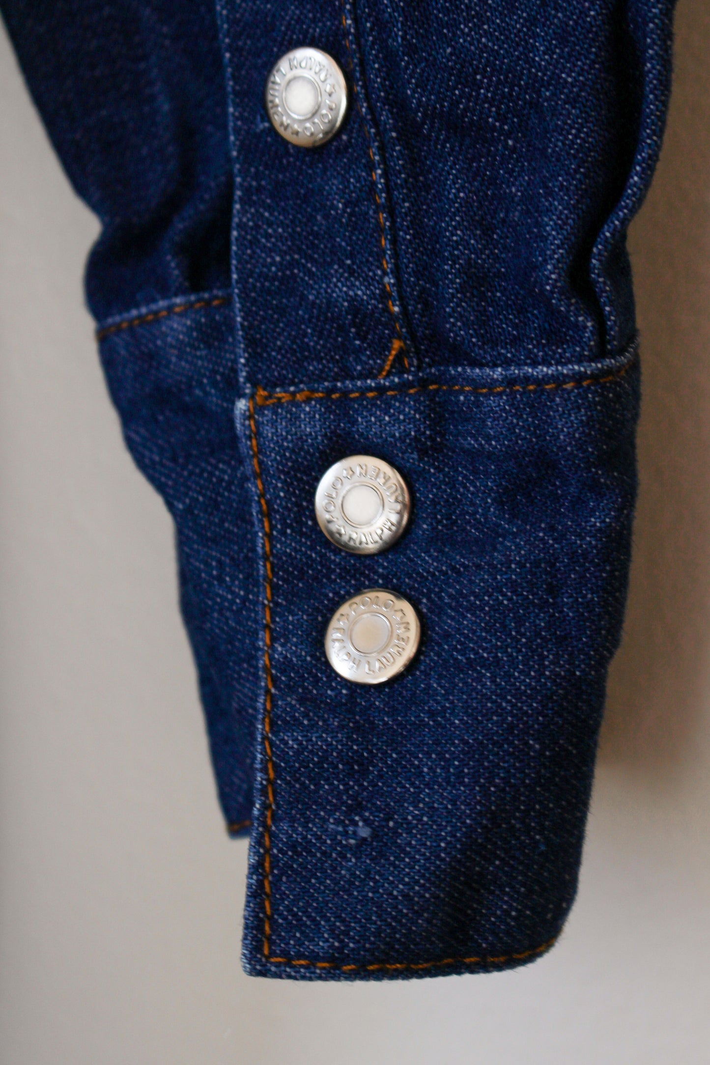 Close-up of blue denim fabric with decorative buttons on a neutral background