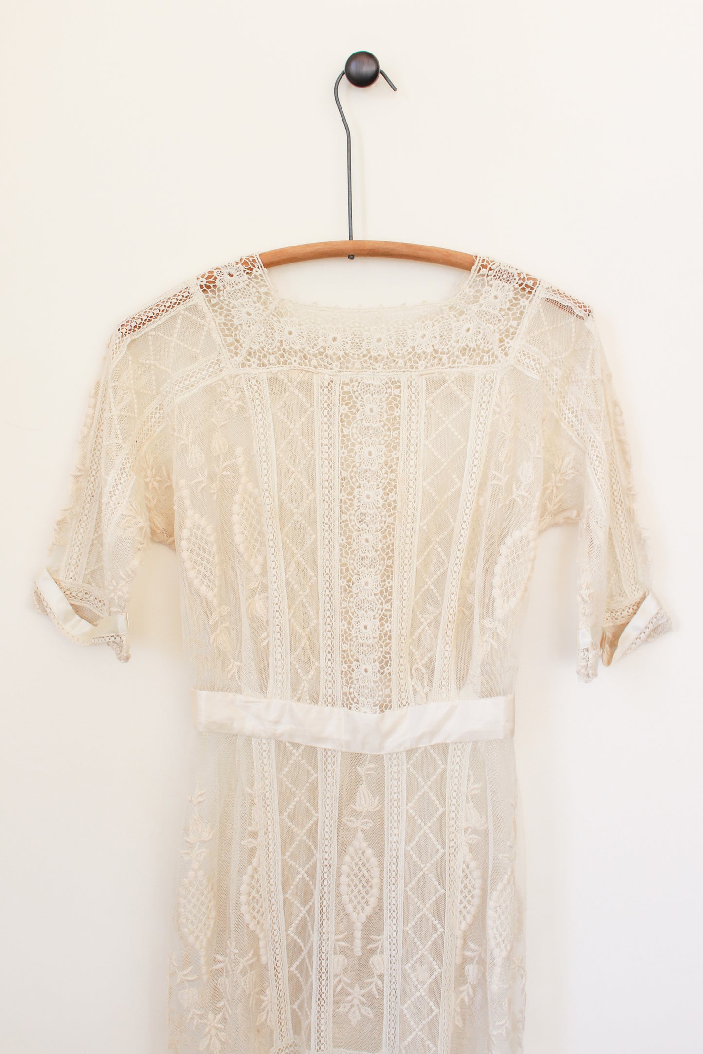 Beige lace top on a wooden hanger against a white background