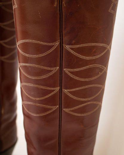 Close-up of brown leather boots with intricate stitching detail on a light background