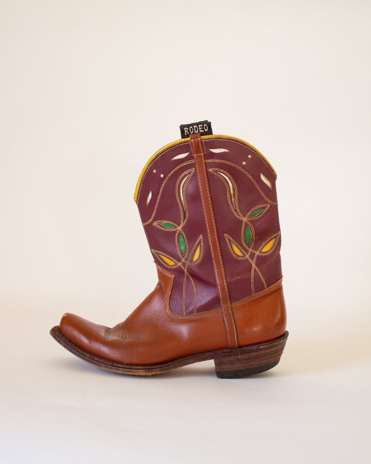 Brown cowboy boot with decorative pattern on a beige background