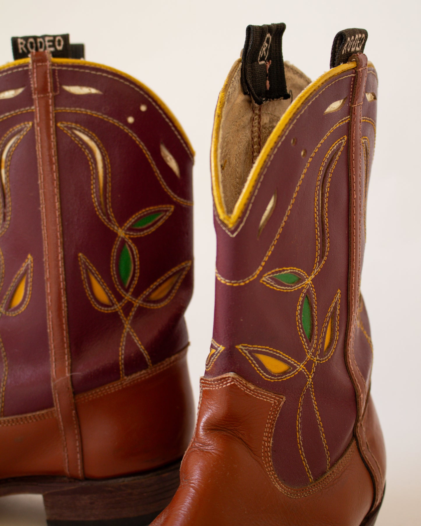 Pair of brown cowboy boots with decorative patterns on a white background