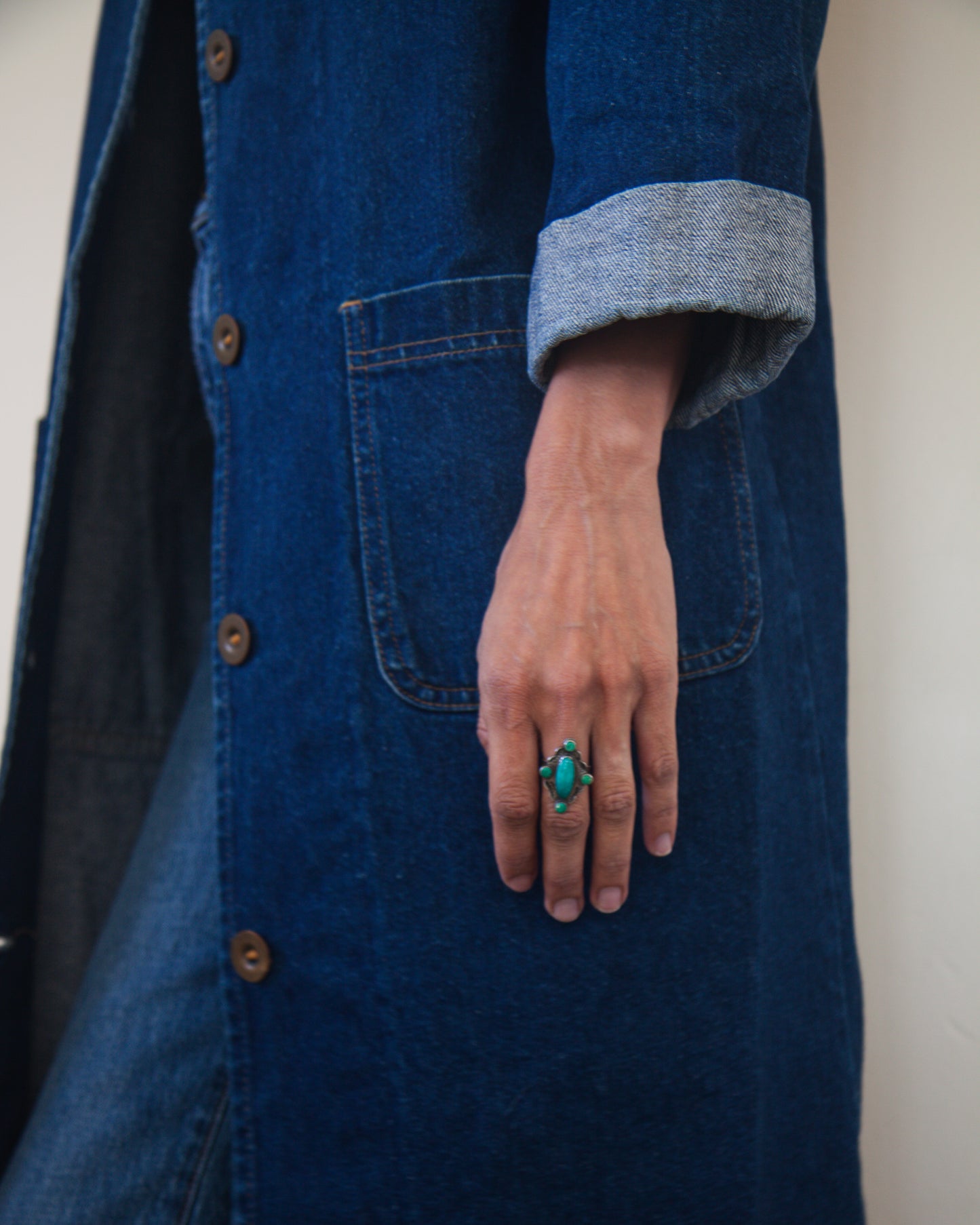 Person wearing a blue coat with a hand in a pocket, wearing a green ring.