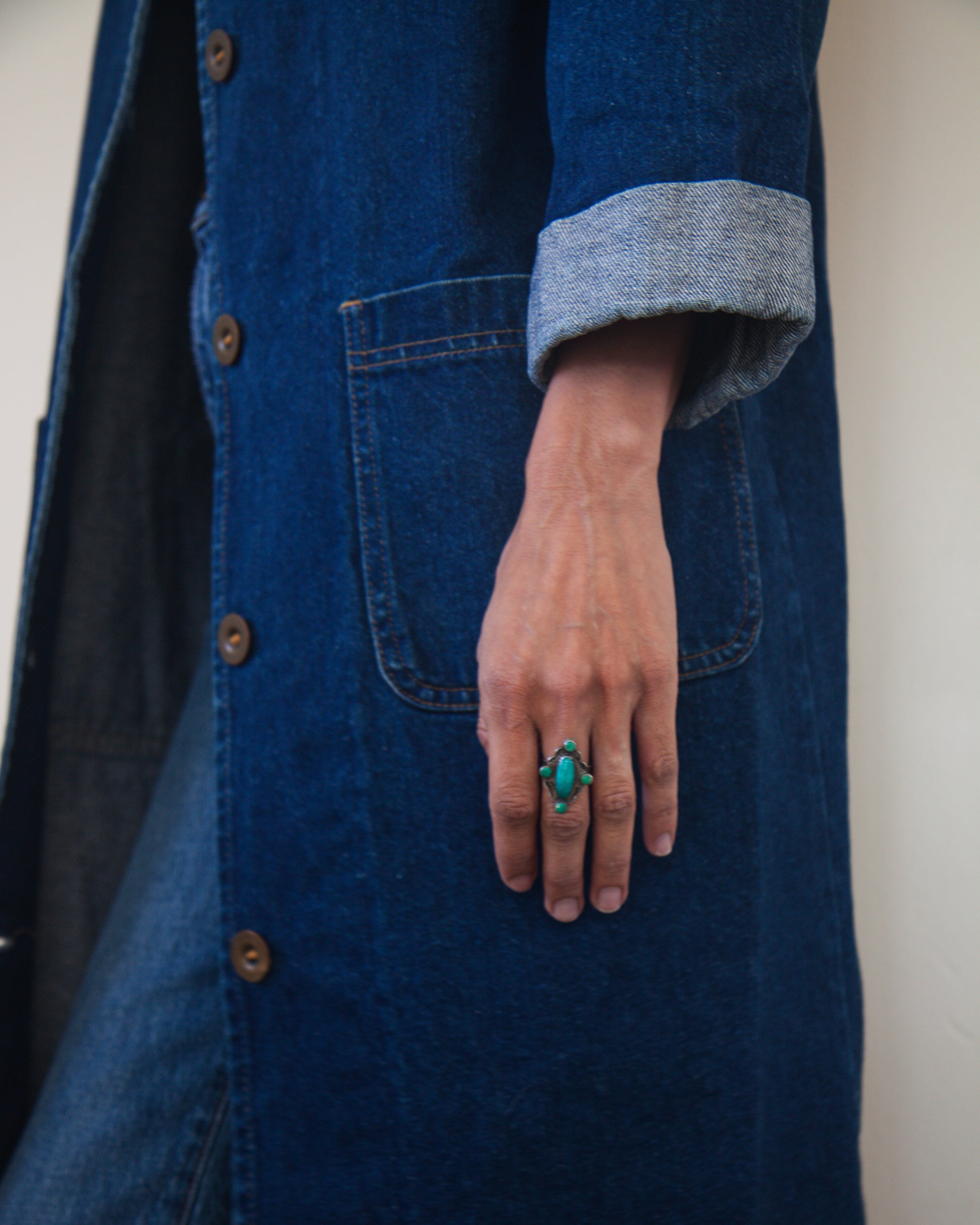 Person wearing a blue coat with a hand in a pocket, wearing a green ring.