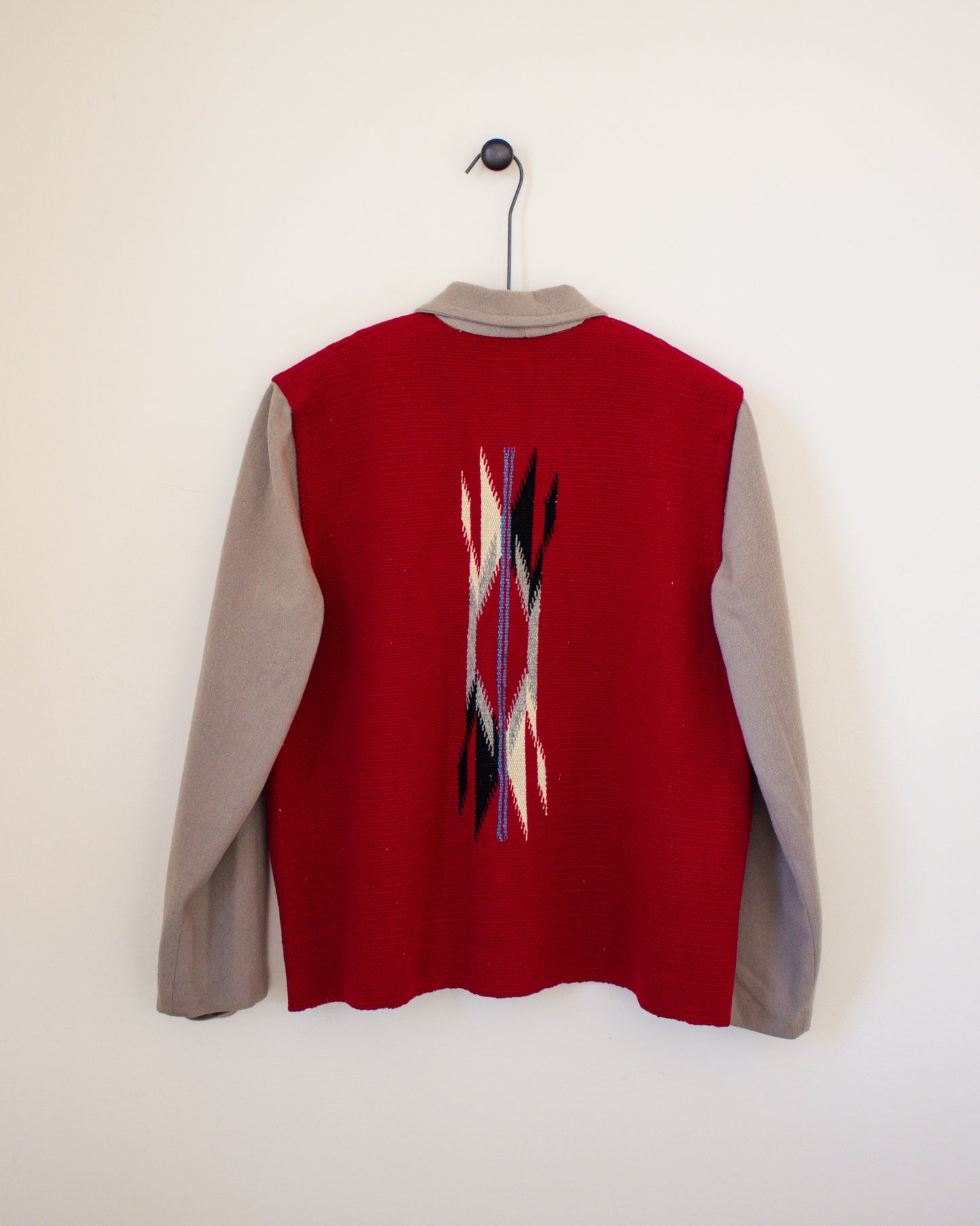 Red and tan jacket with a pattern on the back, hanging against a white background