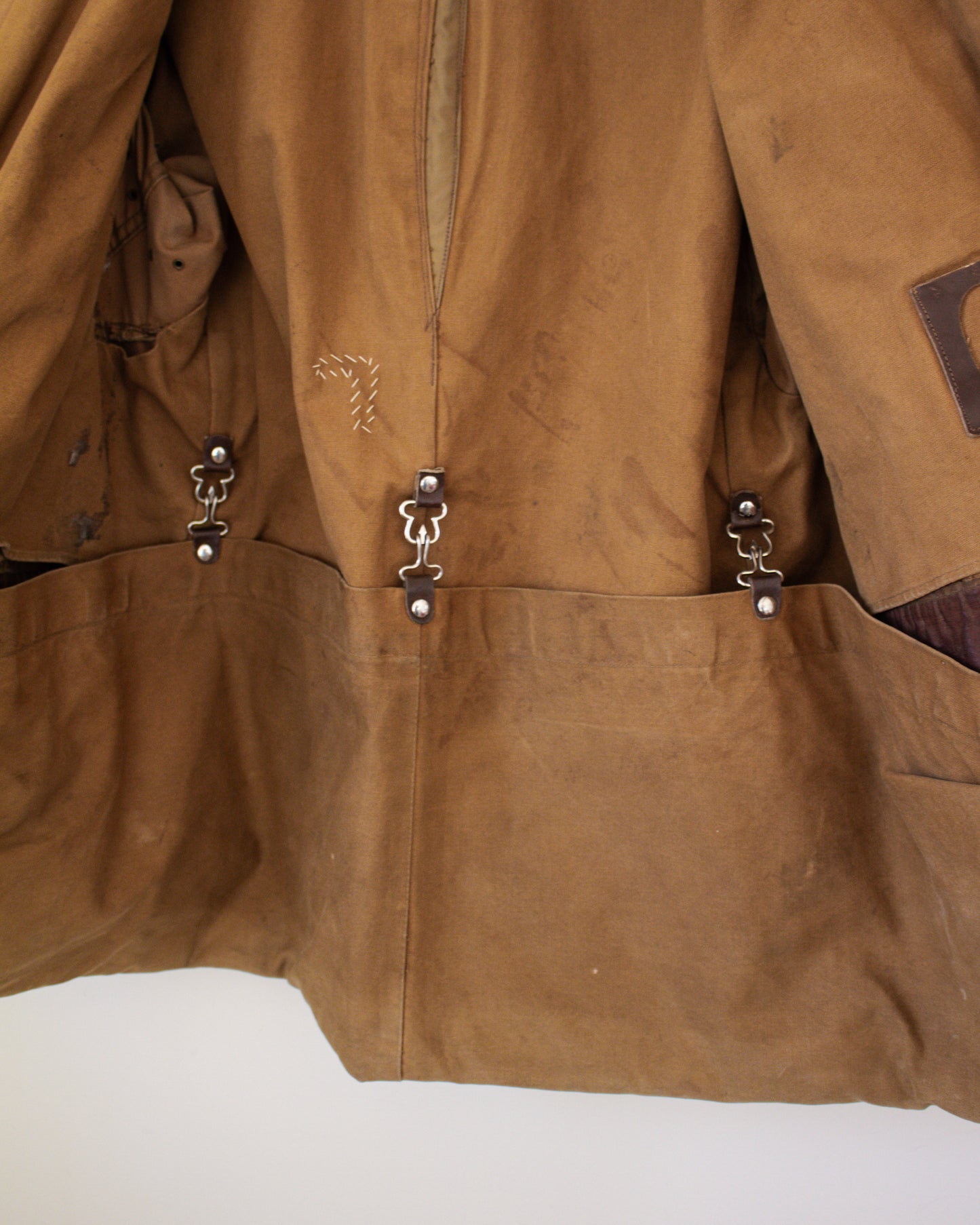 Close-up of backside of a brown canvas jacket with metal clasped pockets on a white background