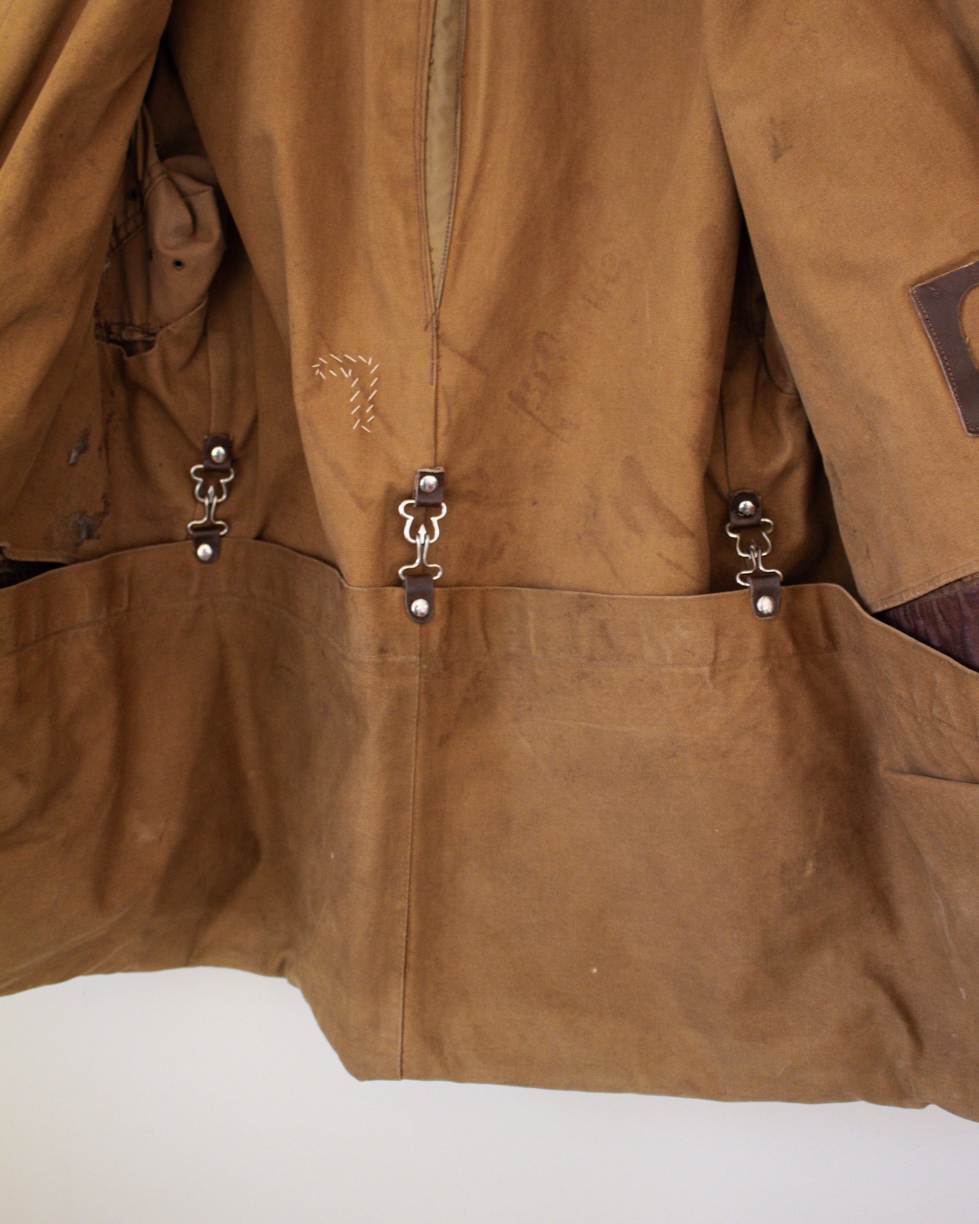 Close-up of backside of a brown canvas jacket with metal clasped pockets on a white background