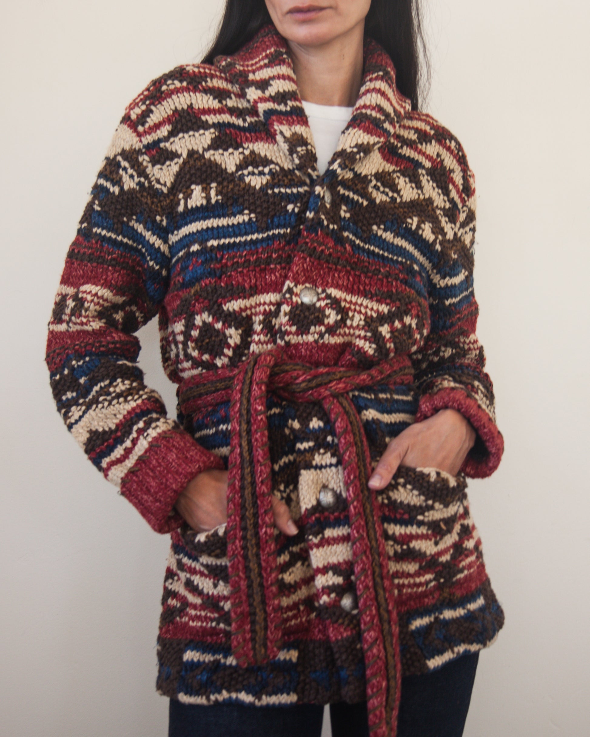 Person wearing a patterned cardigan with a belt on a plain background