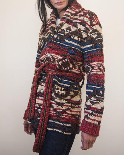 Person wearing a patterned cardigan with a belt on a plain background