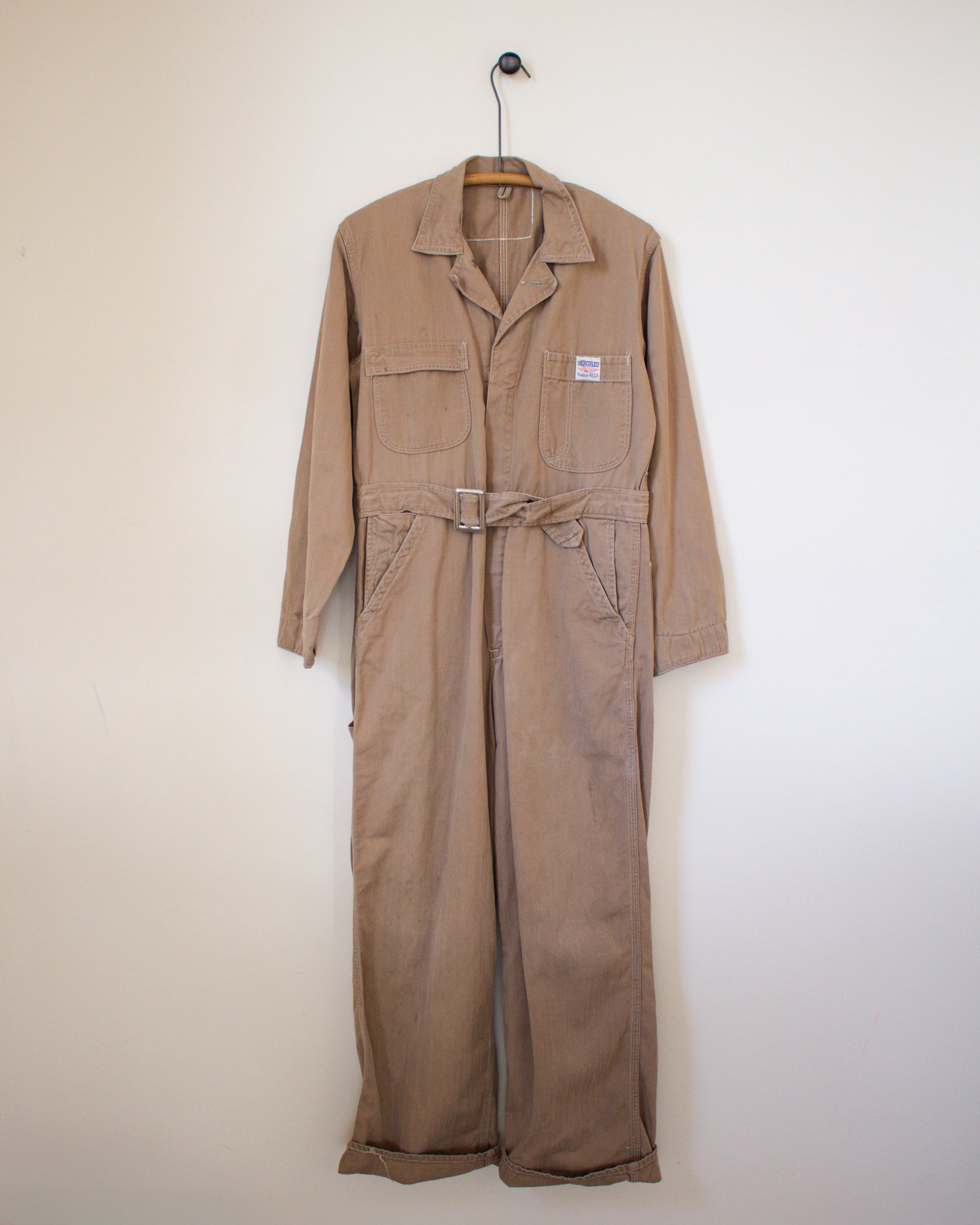 Brown coverall on a hanger against a white wall