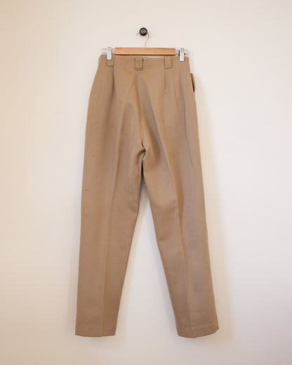 Beige pants hanging on a wooden hanger against a beige wall back view