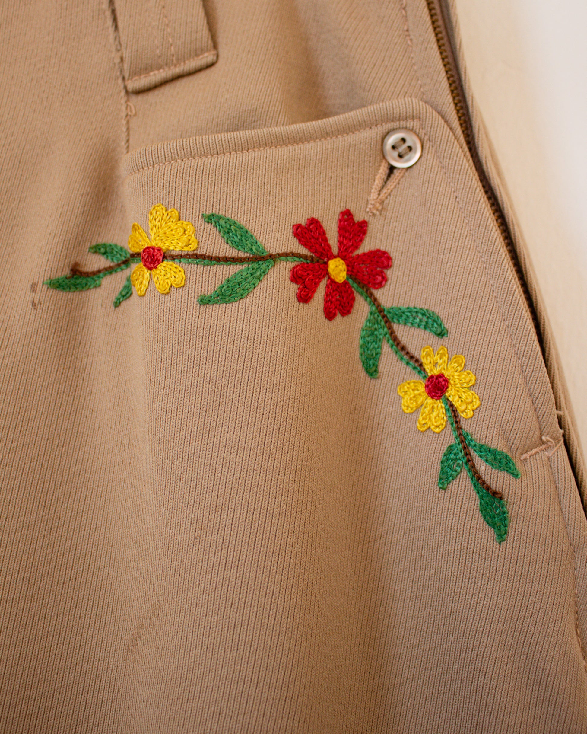 Beige jacket with embroidered red and yellow flowers on a plain background