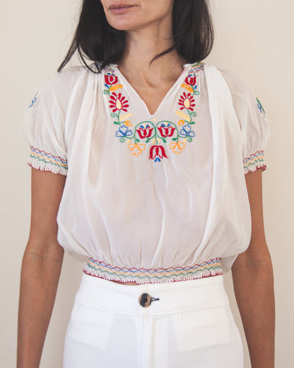 White blouse with colorful embroidery on a plain background