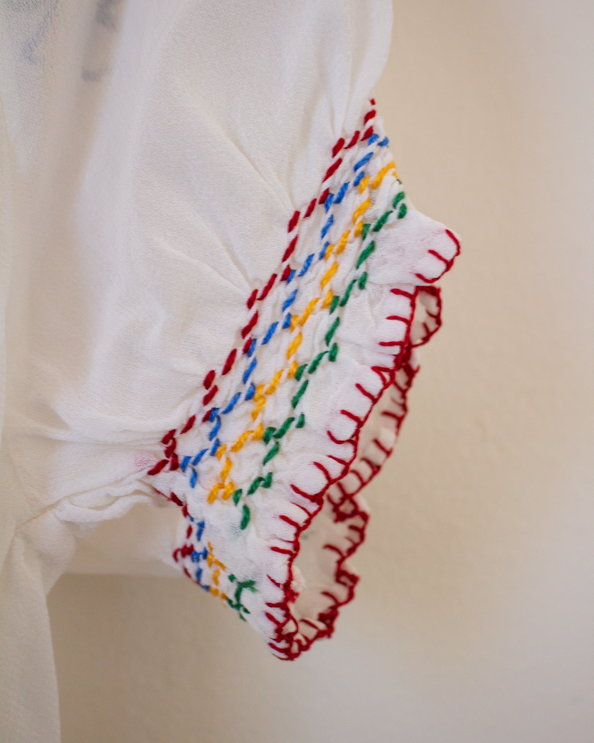 Close-up of a white garment with colorful embroidered trim on a beige background
