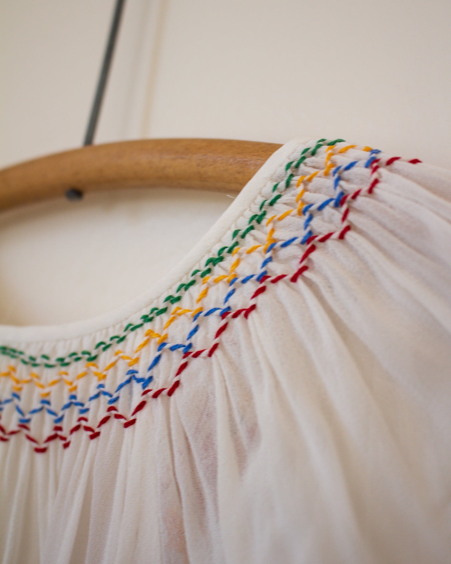 Close-up of a garment with colorful embroidery on a wooden hanger against a light background