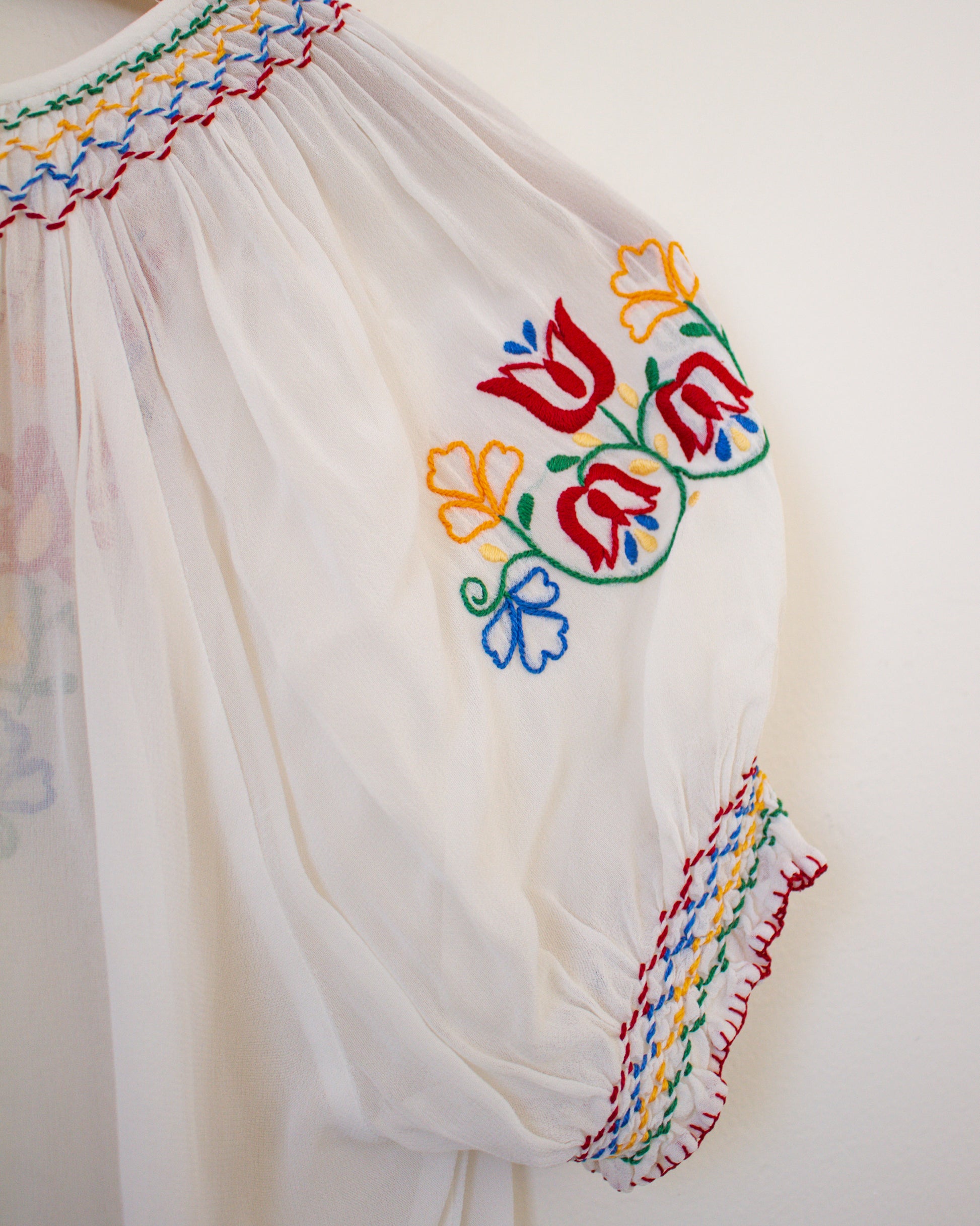 White garment with colorful floral embroidery on a plain background