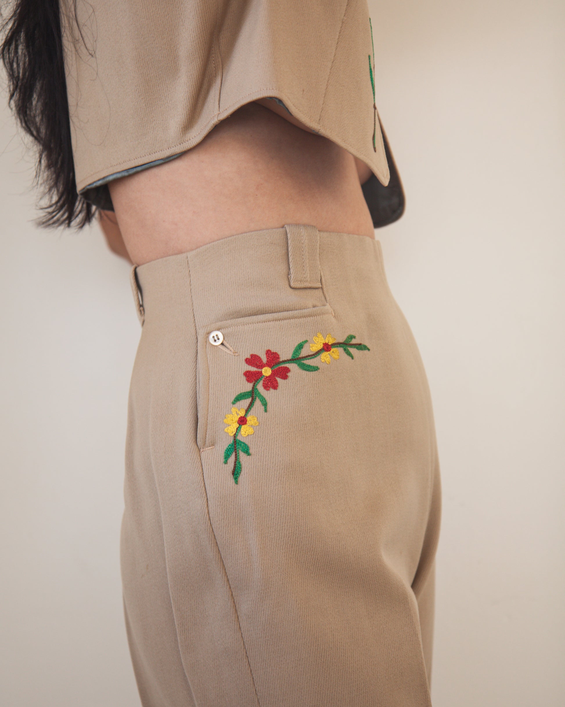 Beige pants with floral embroidery on a plain background