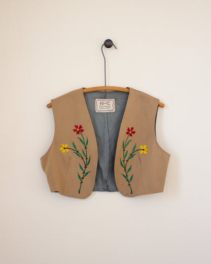 Beige vest with floral embroidery on a hanger against a beige wall