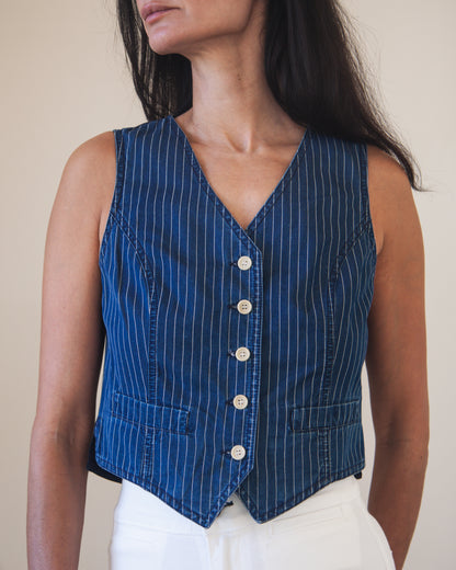 Woman wearing a blue pinstripe vest with white buttons against a neutral background