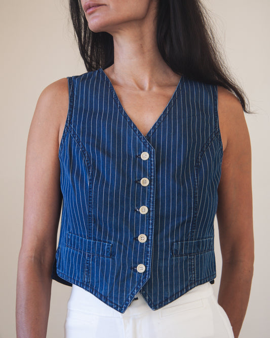 Woman wearing a blue pinstripe vest with white buttons against a neutral background