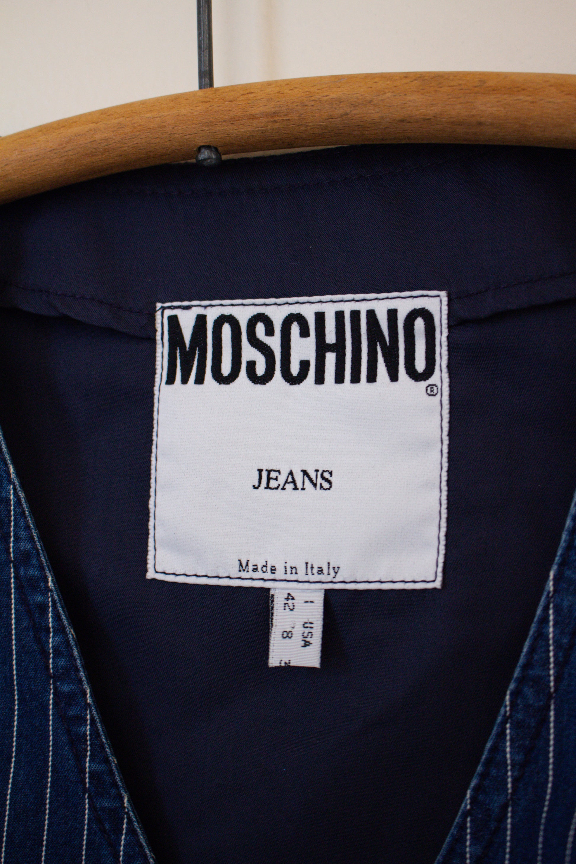 Moschino jeans label on a blue denim garment with a wooden hanger.