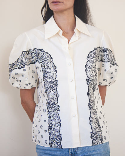 White shirt with black bandana print patterns on sleeves and chest worn by a woman.