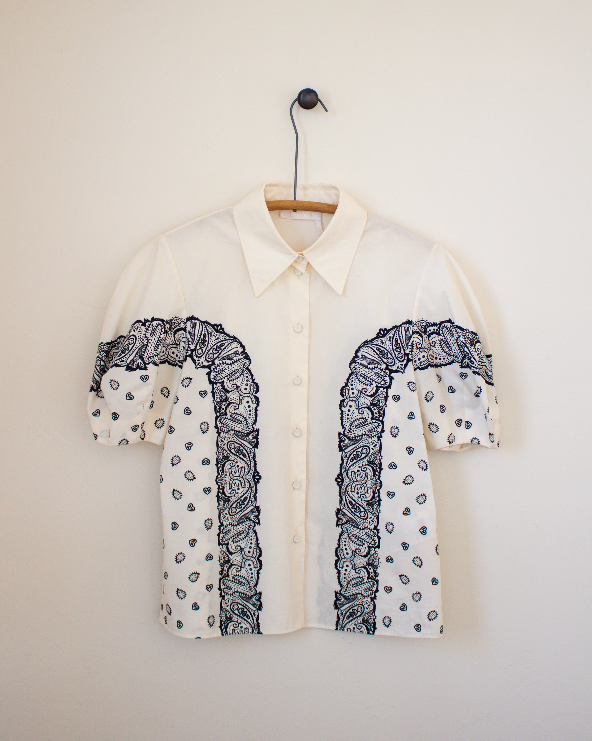 White shirt with black bandana print details on a hanger against a beige wall