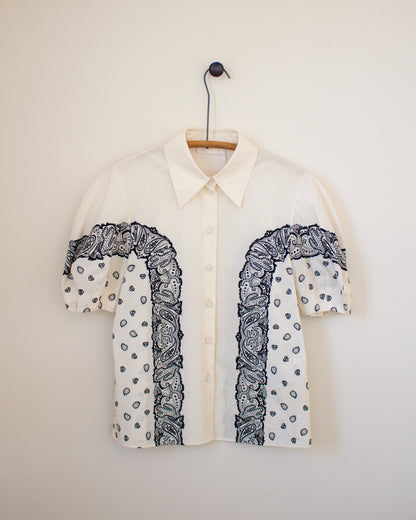 White shirt with black bandana print details on a hanger against a beige wall