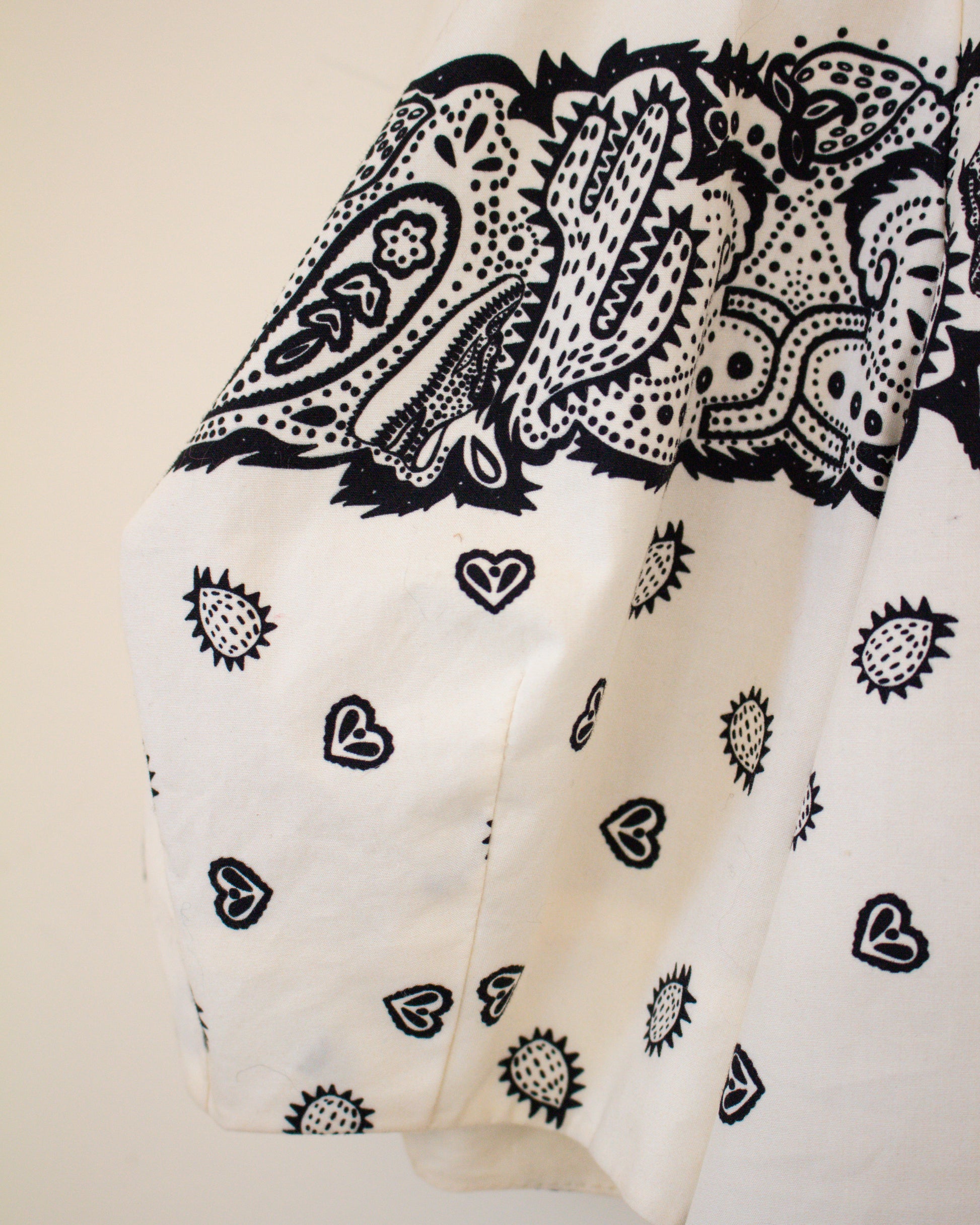 White fabric with black paisley and heart patterns on a beige background