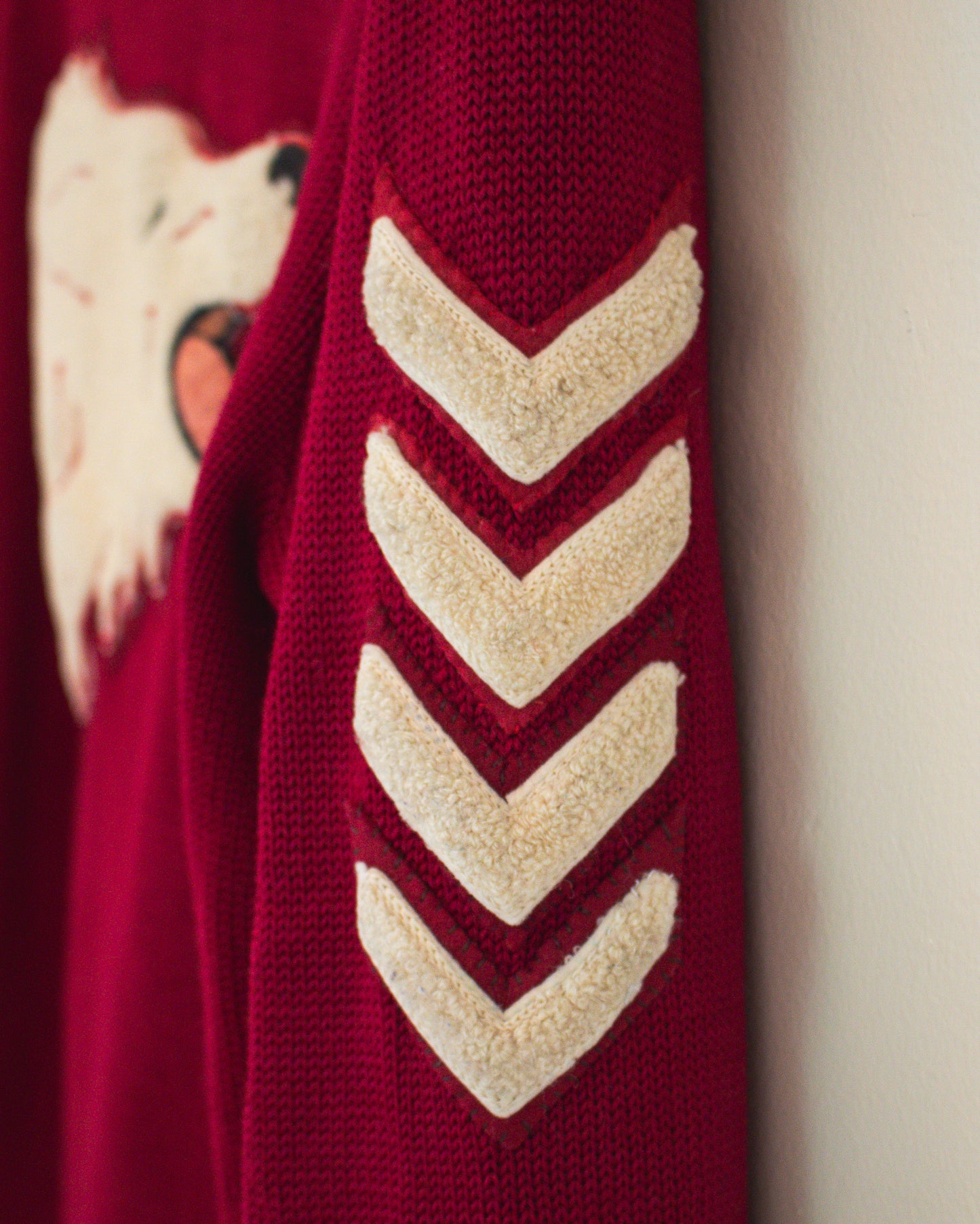 Close-up of a burgundy knit sweater sleeve featuring four cream chevron stripes and part of a white animal face graphic on the upper left.