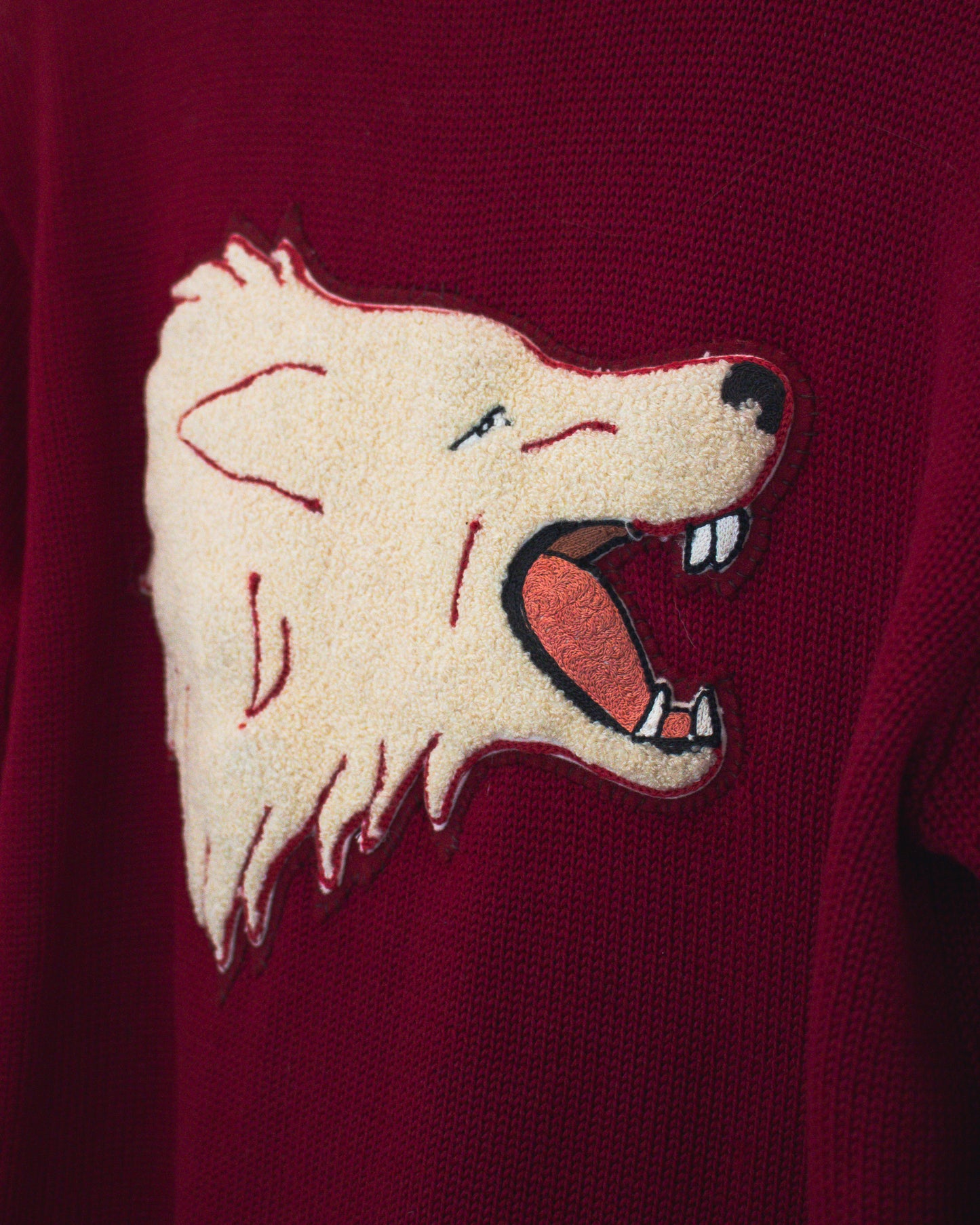 A close-up of a burgundy knit sweater featuring a large embroidered wolf head patch on the chest.