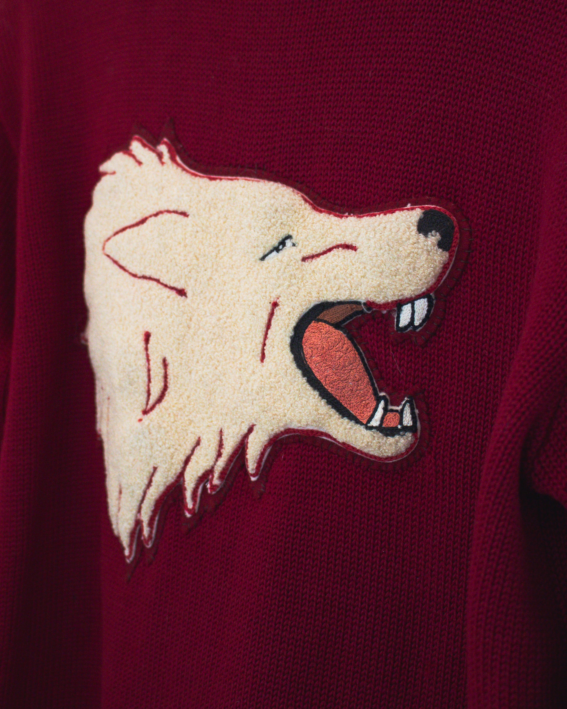 A close-up of a burgundy knit sweater featuring a large embroidered wolf head patch on the chest.