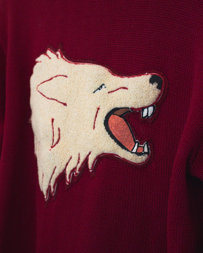 A close-up of a burgundy knit sweater featuring a large embroidered wolf head patch on the chest.