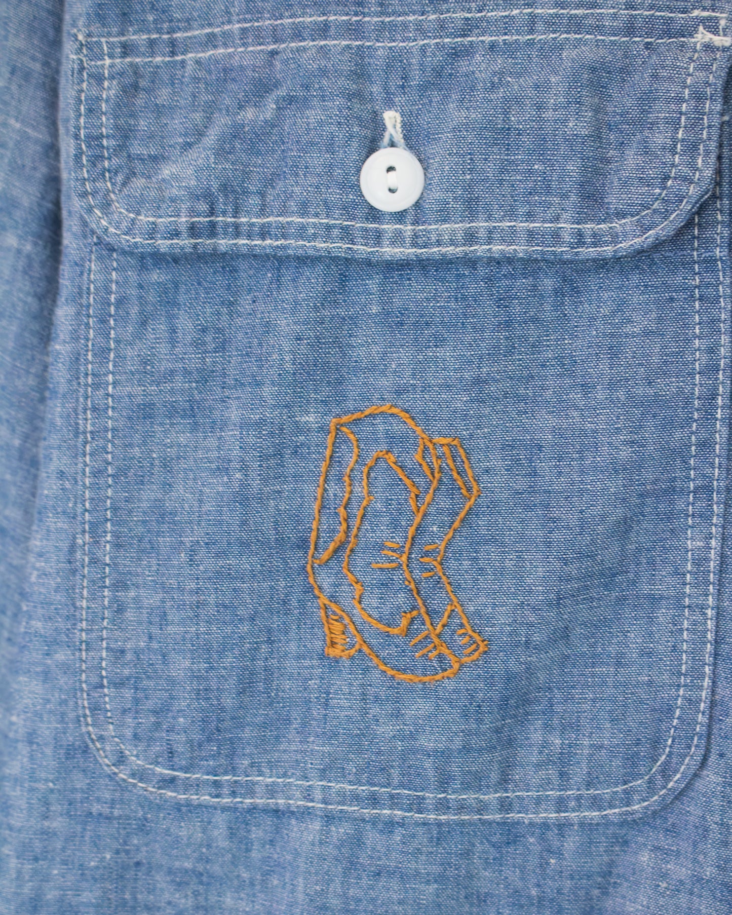 Close-up of a blue denim pocket with a white button and embroidered boots graphic on the front.