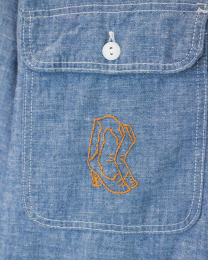 Close-up of a blue denim pocket with a white button and embroidered boots graphic on the front.