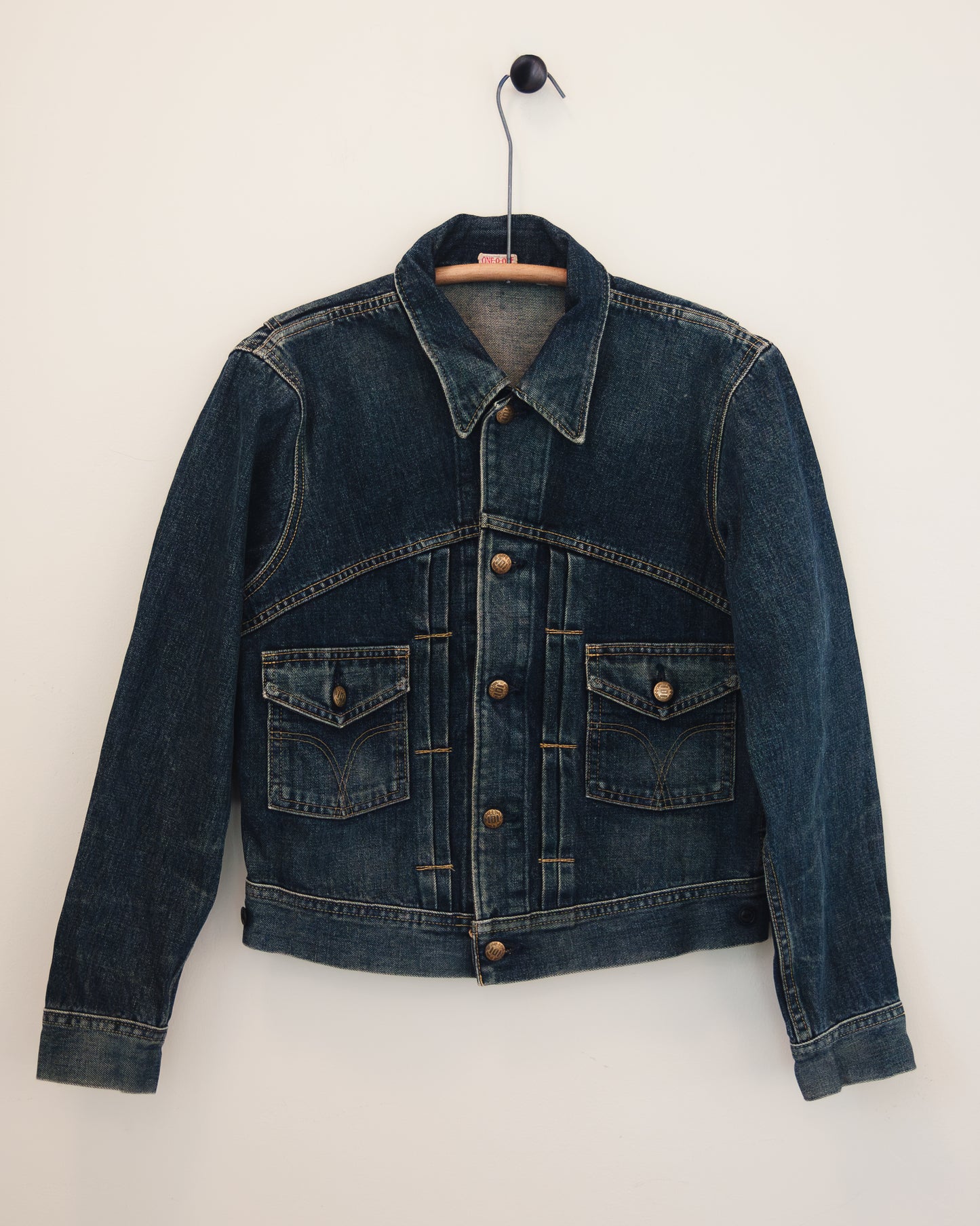 Front of denim jacket with brass buttons on hanger with white background.