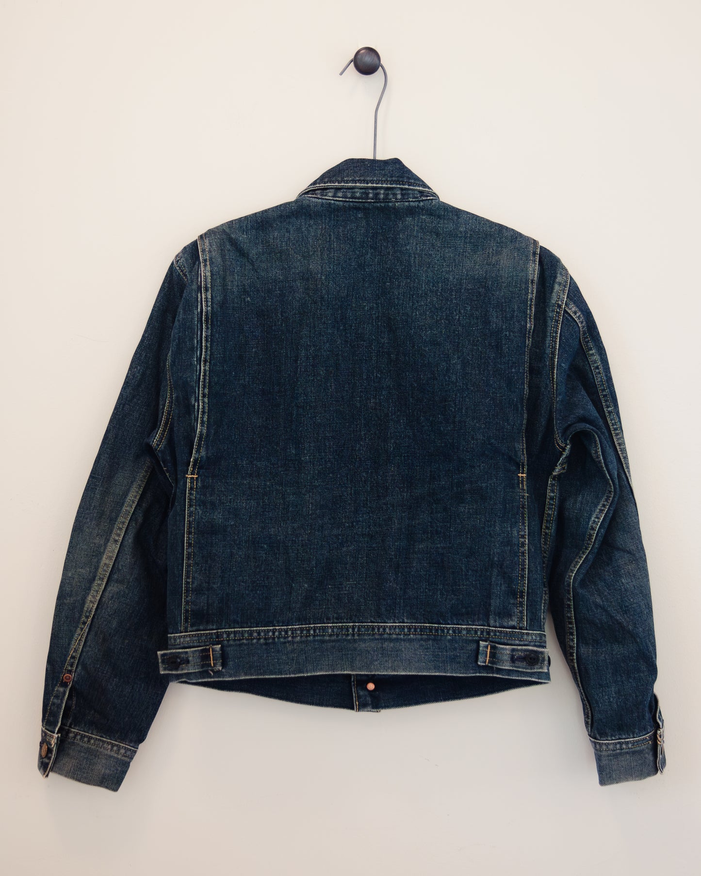Back of denim jacket with brass buttons on hanger with white background.