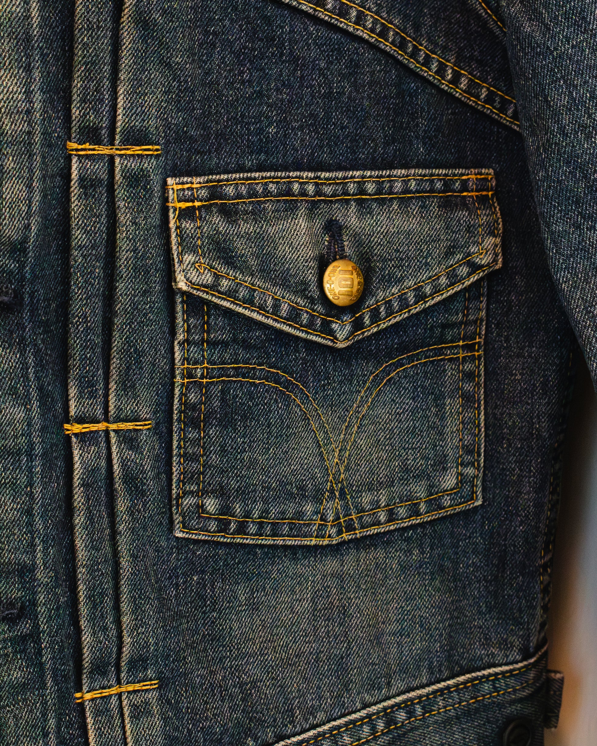 Close-up of front button pocket of denim jacket with brass button.
