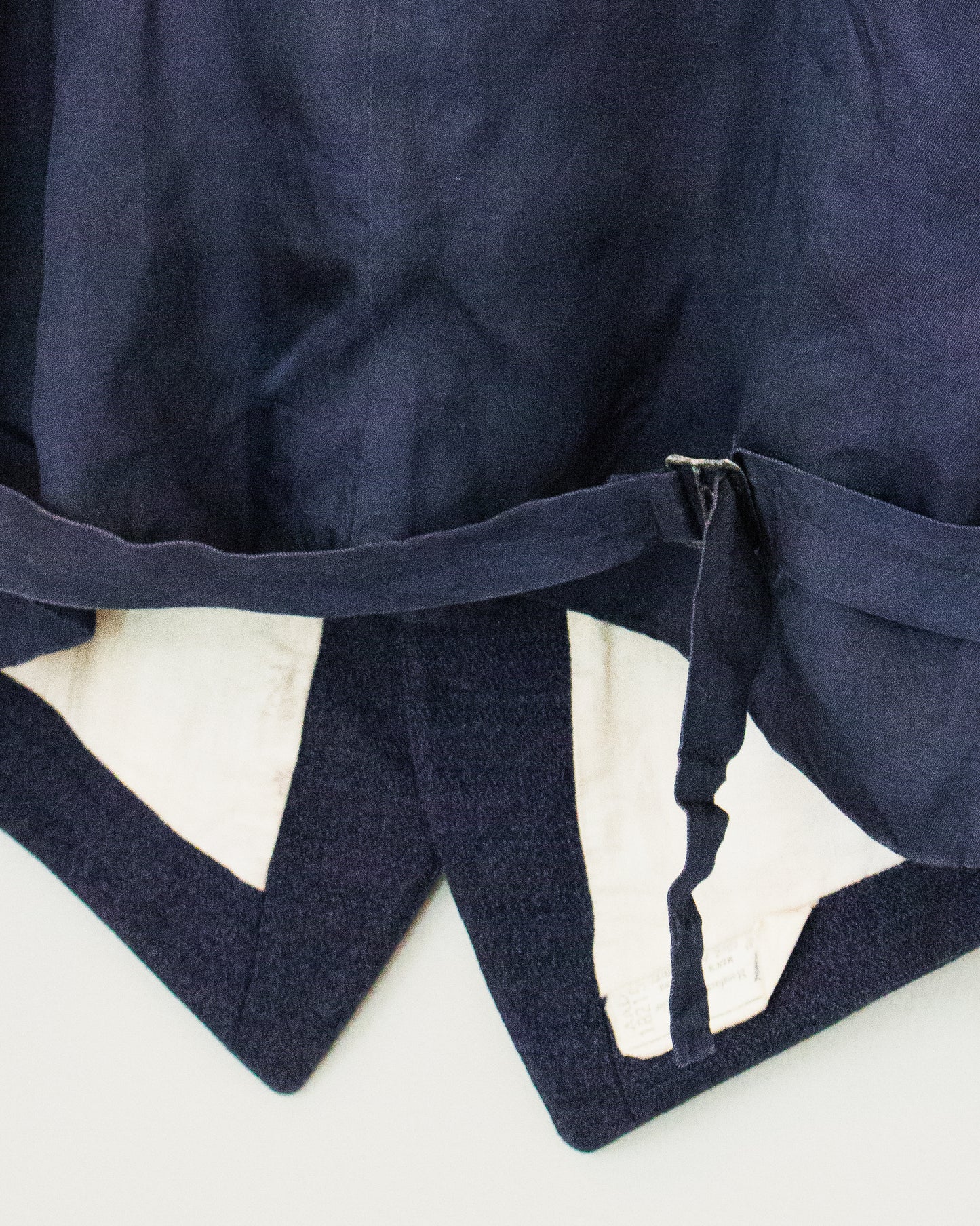 Close-up of a navy blue vest, showing the fabric texture, a belt detail, and a cream-colored lining.