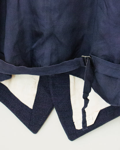 Close-up of a navy blue vest, showing the fabric texture, a belt detail, and a cream-colored lining.