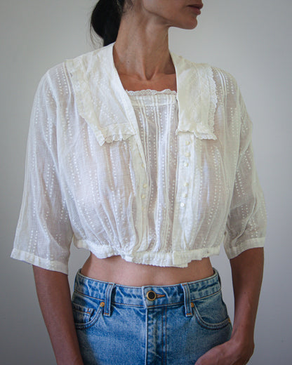 A woman wearing a white blouse with ruffled details, paired with blue jeans.