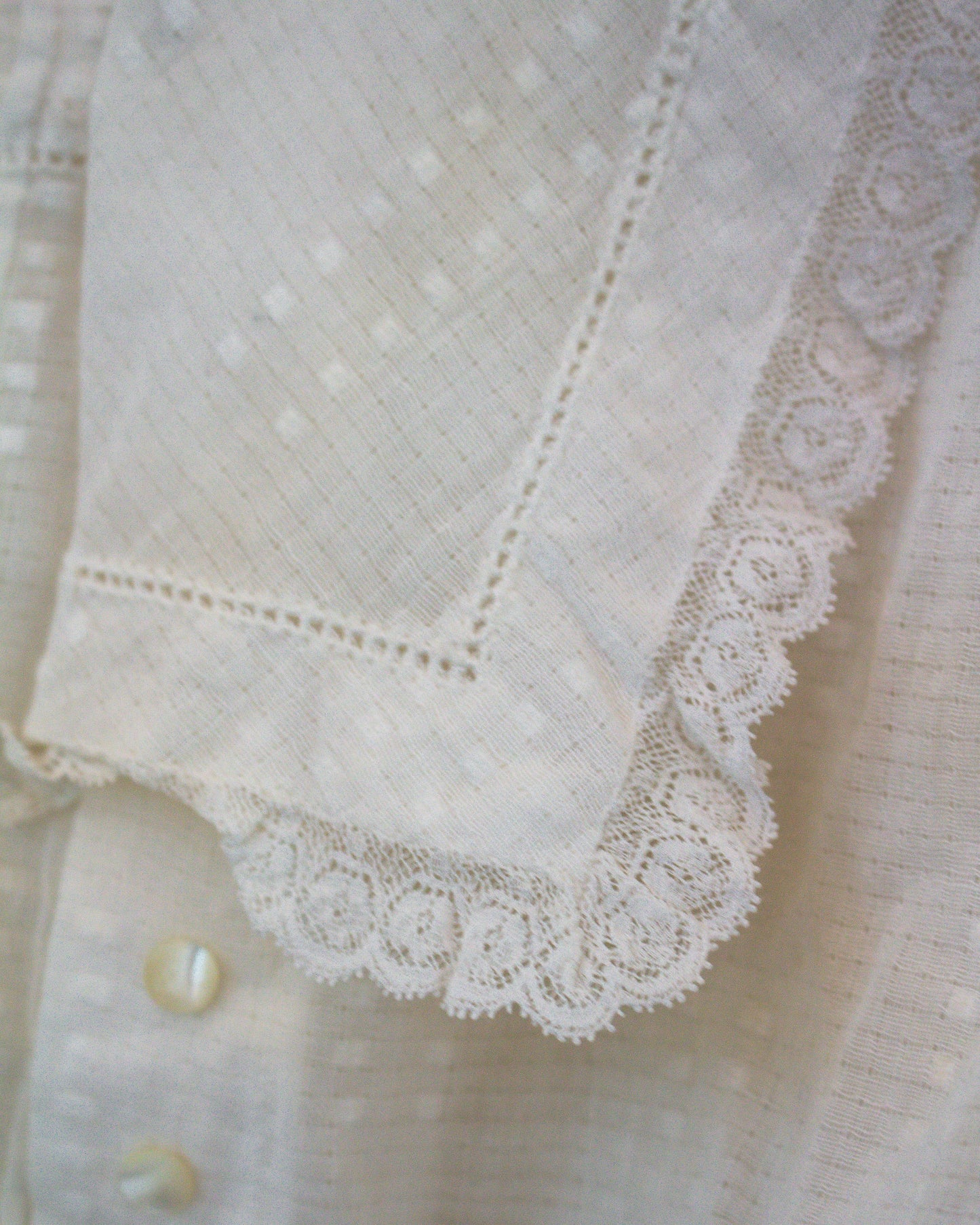 Close-up of a white embroidered cotton collar with scalloped lace trim and eyelet embroidery.