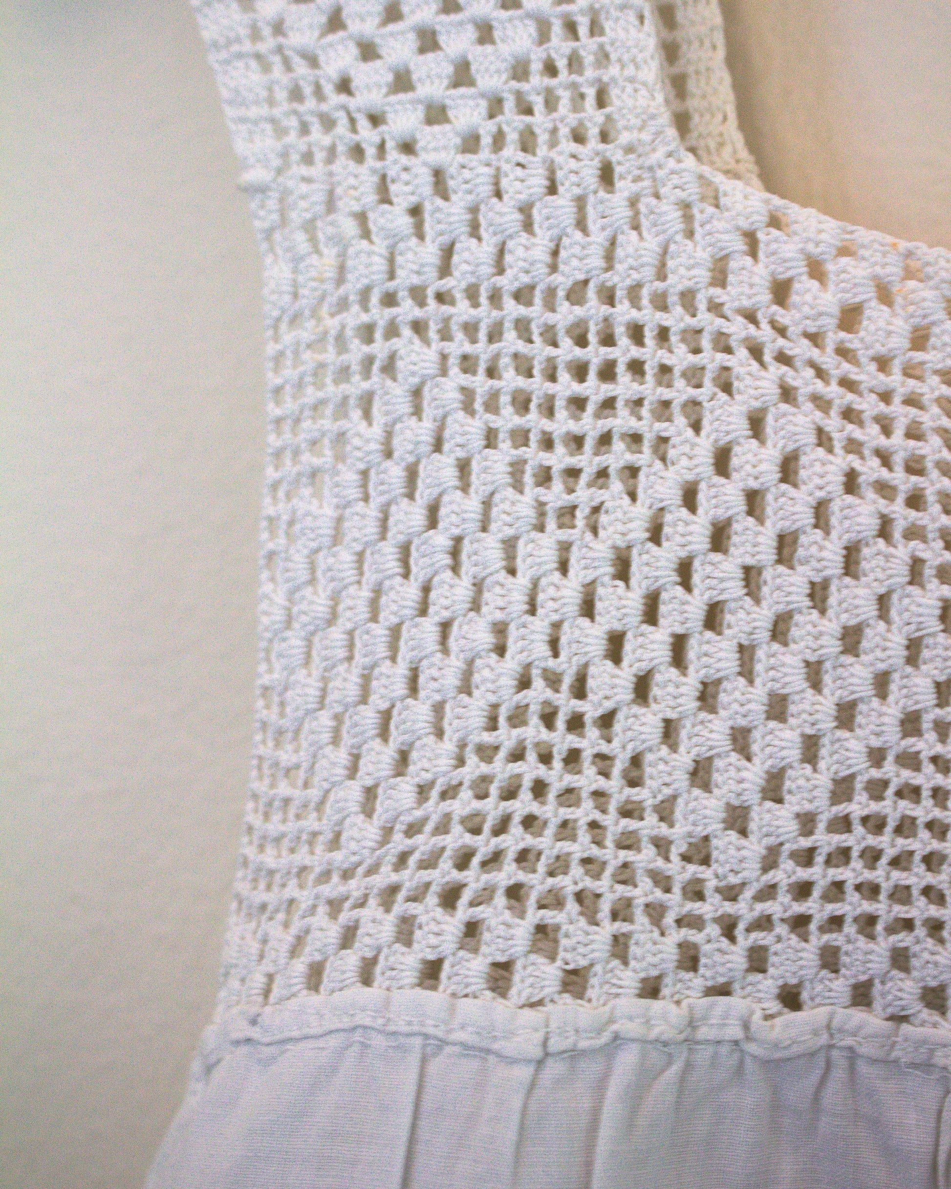 Close-up of a white crocheted sleeveless top against a plain light background.