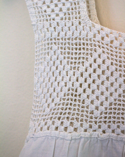 Close-up of a white crocheted sleeveless top against a plain light background.