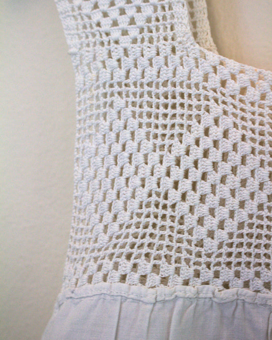 Close-up of a white crocheted sleeveless top against a plain light background.