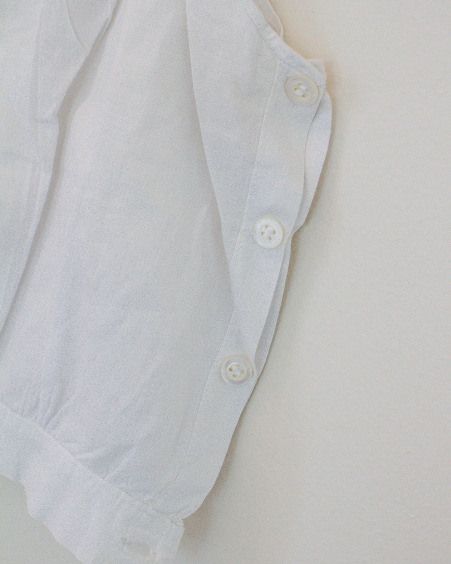 Close-up of a white garment, showing the side buttons and a portion of the fabric against a plain light background.