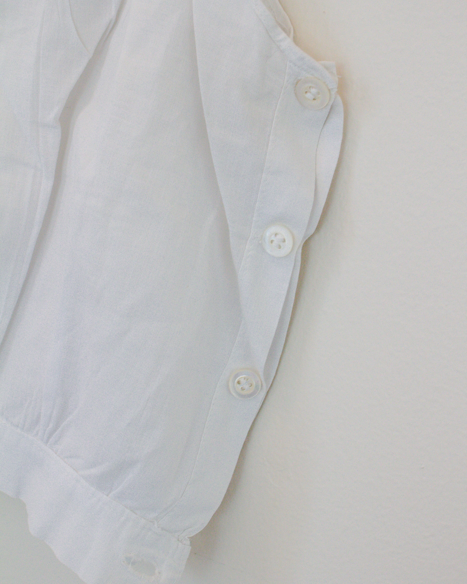 Close-up of a white garment, showing the side buttons and a portion of the fabric against a plain light background.